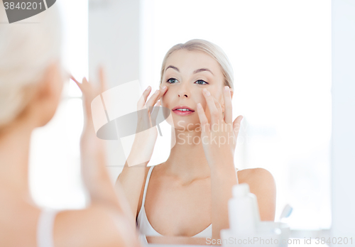 Image of happy woman applying cream to face at bathroom