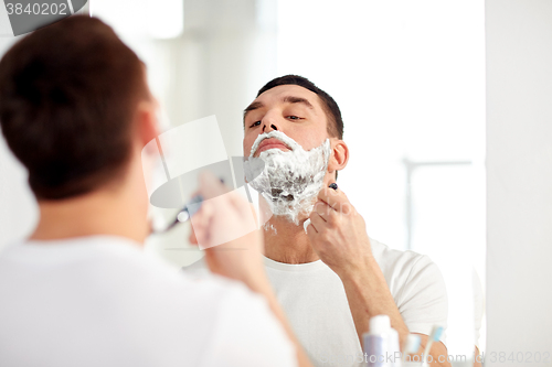 Image of man shaving beard with razor blade at bathroom