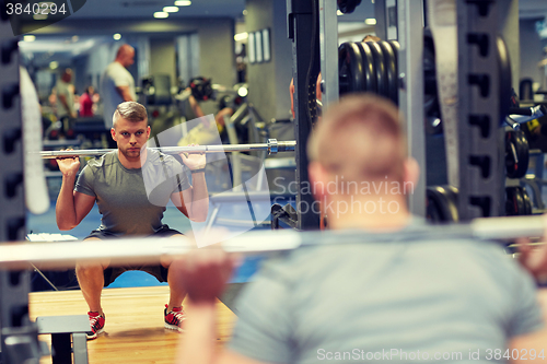 Image of young man flexing muscles with barbell in gym