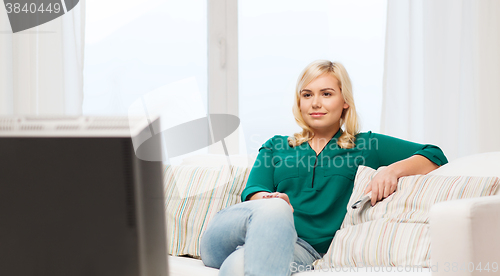 Image of smiling woman with remote watching tv at home