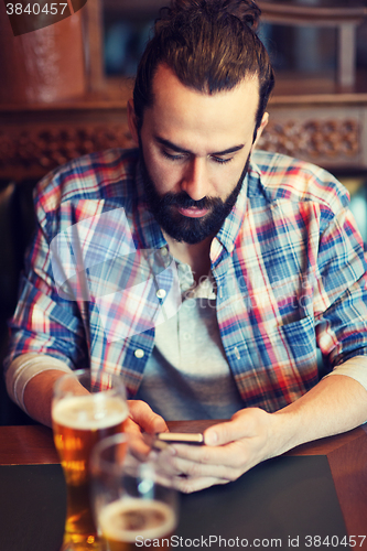 Image of man with smartphone drinking beer at bar