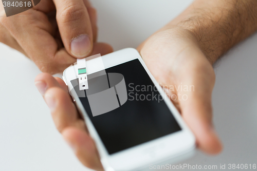 Image of close up of man with smartphone making blood test