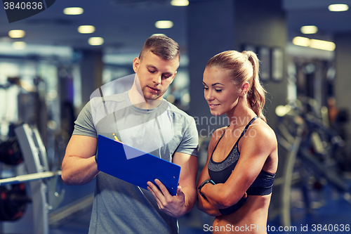 Image of smiling young woman with personal trainer in gym