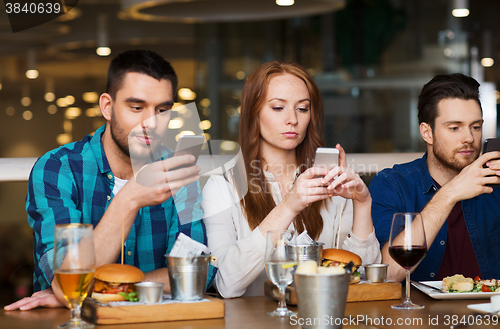Image of friends with smartphones dining at restaurant