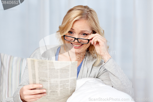 Image of woman in eyeglasses reading newspaper at home