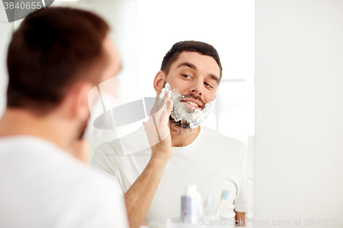 Image of happy man applying shaving foam at bathroom mirror