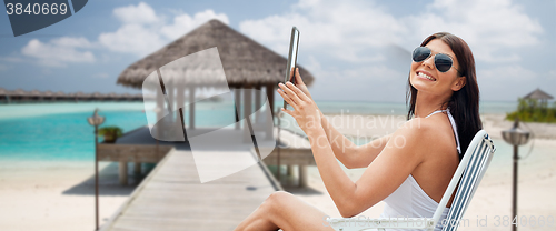 Image of smiling woman with tablet pc sunbathing on beach