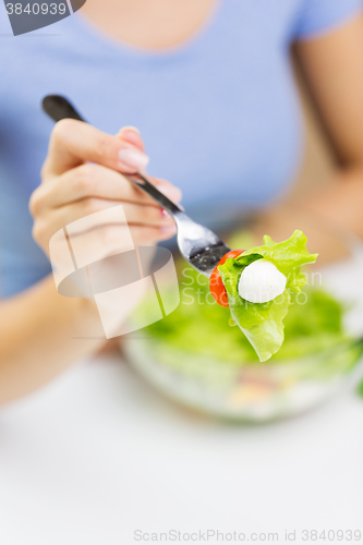 Image of close up of young woman eating salad at home