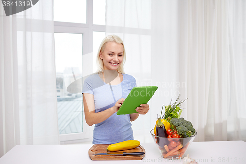 Image of smiling young woman with tablet pc cooking at home