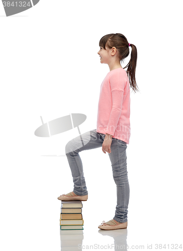 Image of happy little girl stepping on book pile