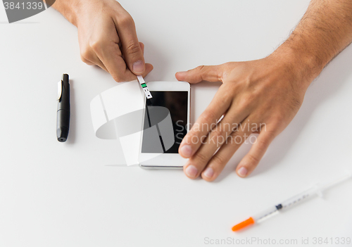 Image of close up of man with smartphone making blood test