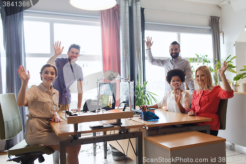 Image of happy creative team waving hands in office