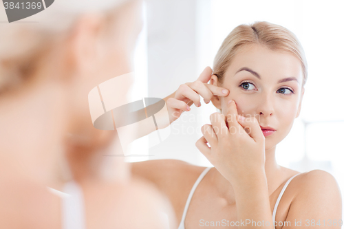 Image of woman squeezing pimple at bathroom mirror