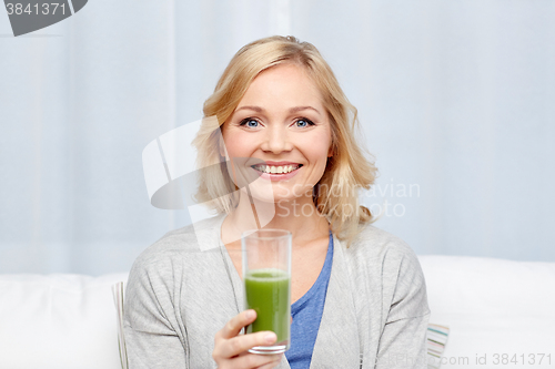 Image of happy woman drinking green juice or shake at home