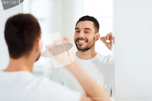 Image of man cleaning ear with cotton swab at bathroom