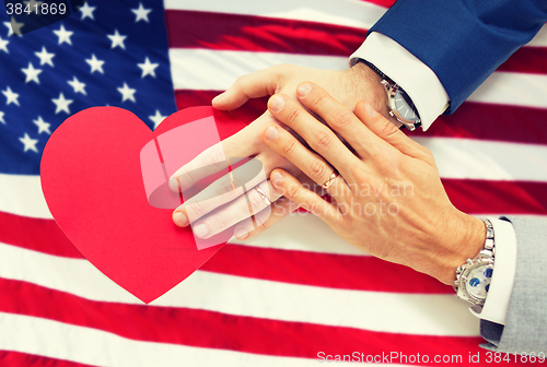 Image of close up of male gay couple hands with red heart