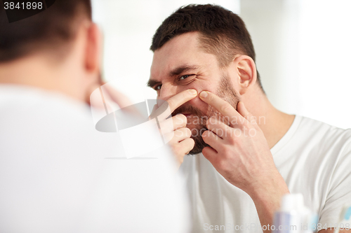 Image of man squeezing pimple at bathroom mirror