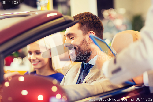 Image of happy couple with car dealer in auto show or salon