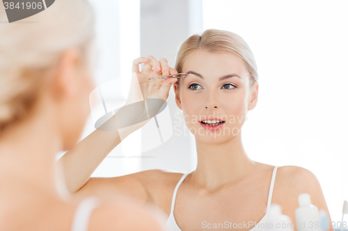 Image of woman with tweezers tweezing eyebrow at bathroom
