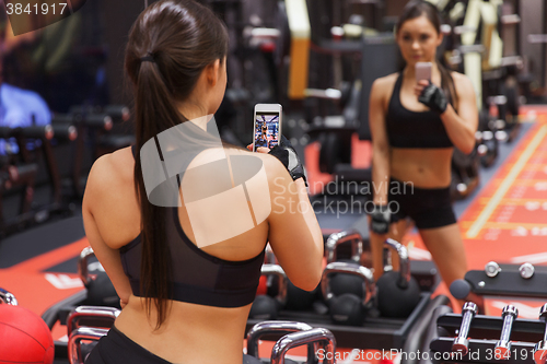 Image of woman with smartphone taking mirror selfie in gym