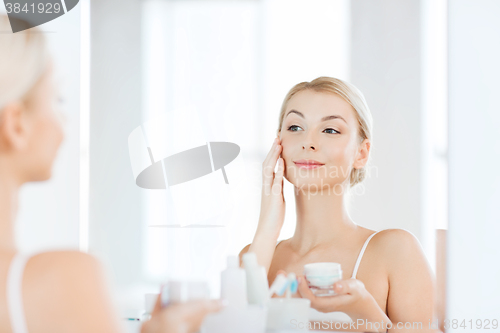 Image of happy woman applying cream to face at bathroom