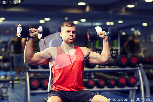 Image of young man with dumbbells flexing muscles in gym