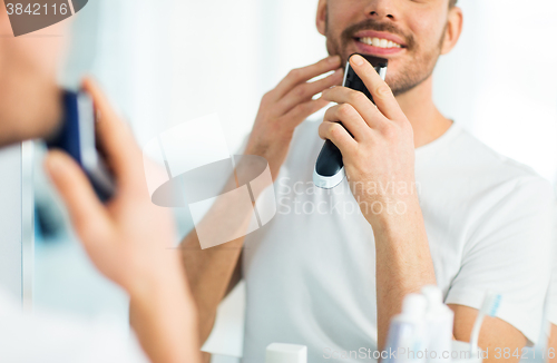 Image of close up of man shaving beard with trimmer