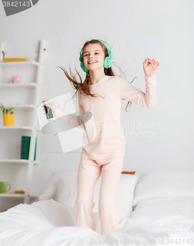 Image of girl jumping on bed with smartphone and headphones