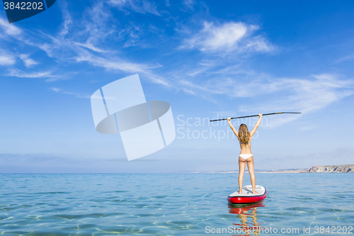 Image of A beautiful and happy woman with arms up and learning paddle-sur
