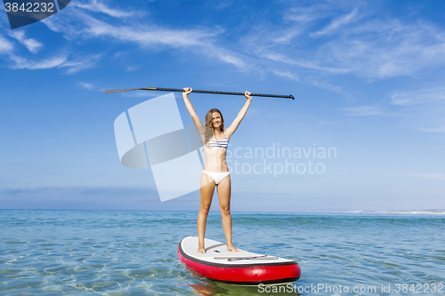 Image of A beautiful and happy woman with arms up and learning paddle-sur