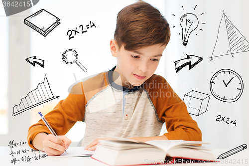 Image of student boy with book writing to notebook at home