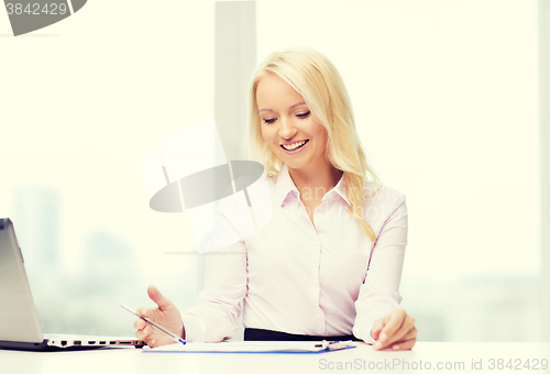 Image of smiling businesswoman reading papers in office