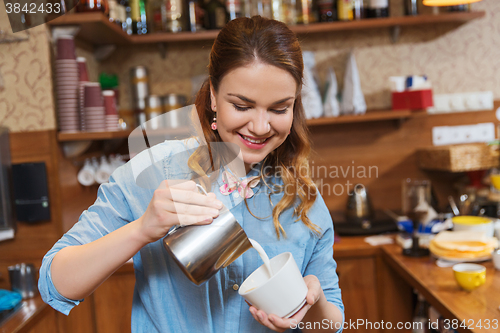 Image of barista woman pouring cream to cup at coffee shop