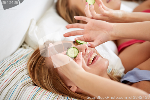 Image of happy young women with cucumber mask lying in bed