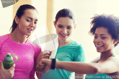 Image of happy women showing time on wrist watch in gym