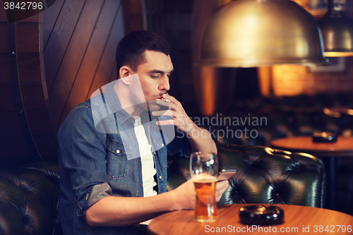 Image of man drinking beer and smoking cigarette at bar