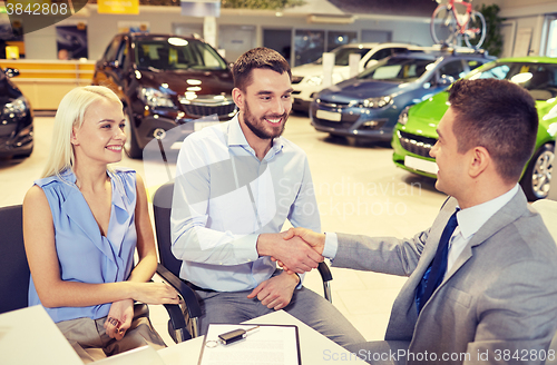 Image of happy couple with car dealer in auto show or salon