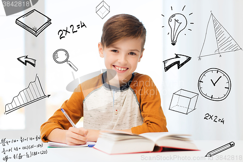 Image of smiling student boy writing to notebook at home