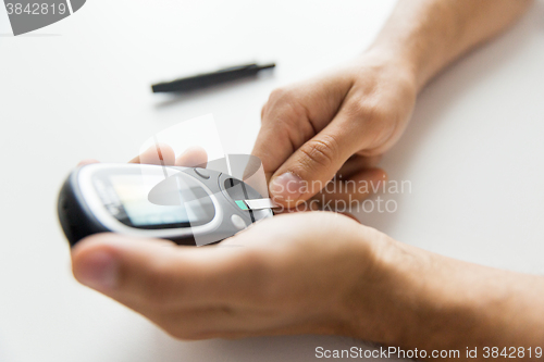 Image of close up of man checking blood sugar by glucometer