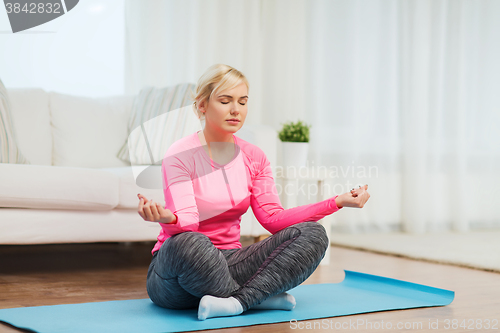 Image of happy woman stretching leg on mat at home