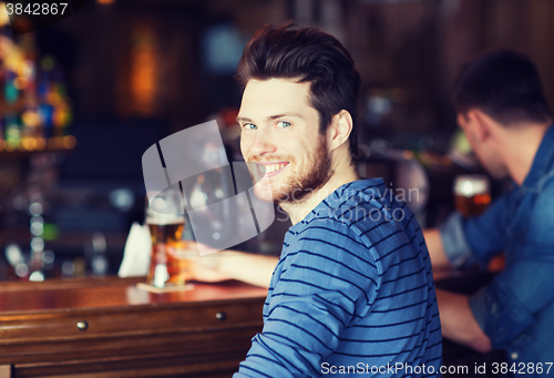 Image of happy young man drinking beer at bar or pub