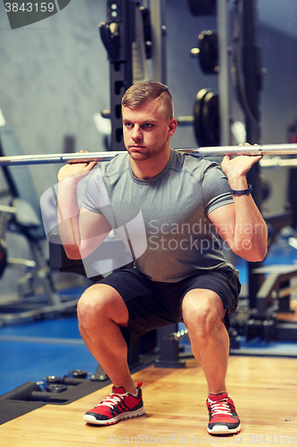 Image of young man flexing muscles with barbell in gym