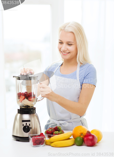 Image of smiling woman with blender preparing shake at home