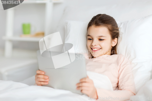 Image of happy girl lying in bed with tablet pc at home