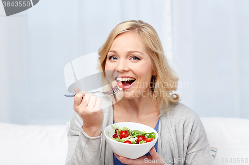 Image of smiling middle aged woman eating salad at home
