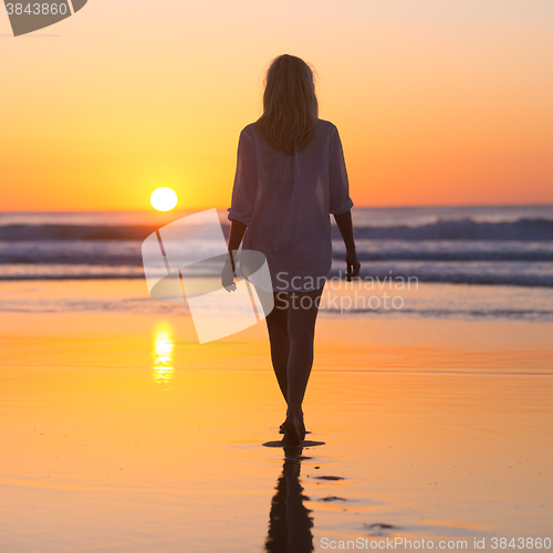 Image of Lady walking on sandy beach in sunset.