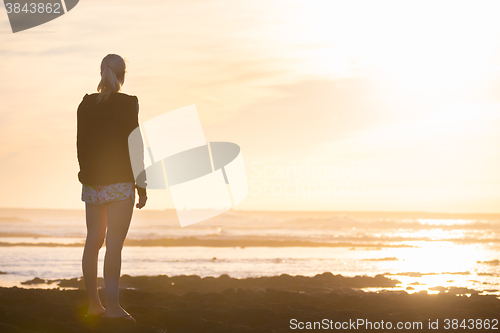 Image of Woman on sandy beach watching sunset.