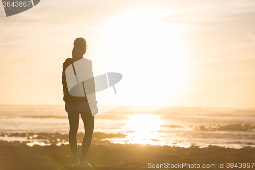 Image of Woman on sandy beach watching sunset.