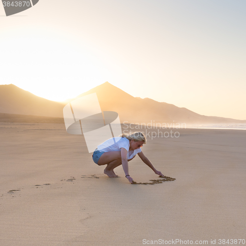 Image of Lady drawing heart shape in sand on beach.