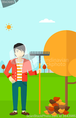 Image of Man with rake standing near tree and heap of autumn leaves.